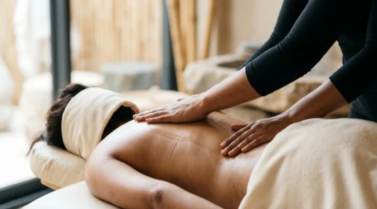 Mains de massothérapeute effectuant un effleurage sur le dos d'un patient dans une ambiance apaisante